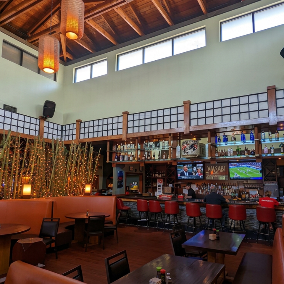 Spacious Japanese restaurant interior with glowing bamboo decor, red bar stools, liquor shelves, televisions, and diners.